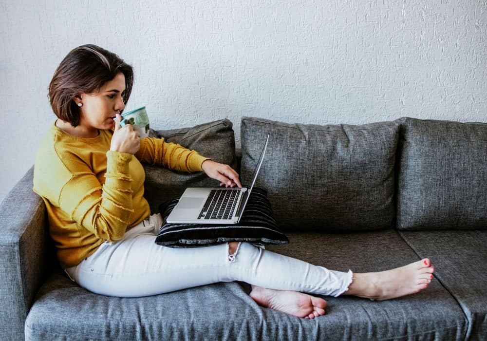 Person sitting on a couch with laptop and cup of tea, ready for their first Telehealth session.