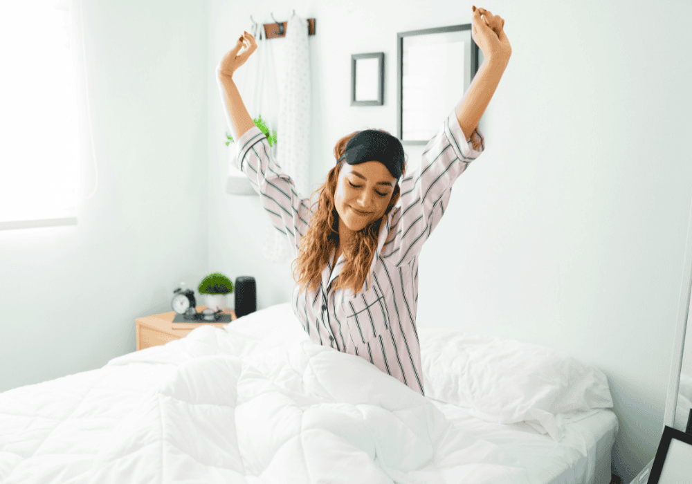 Woman smiling and sitting up in bed with arms in air